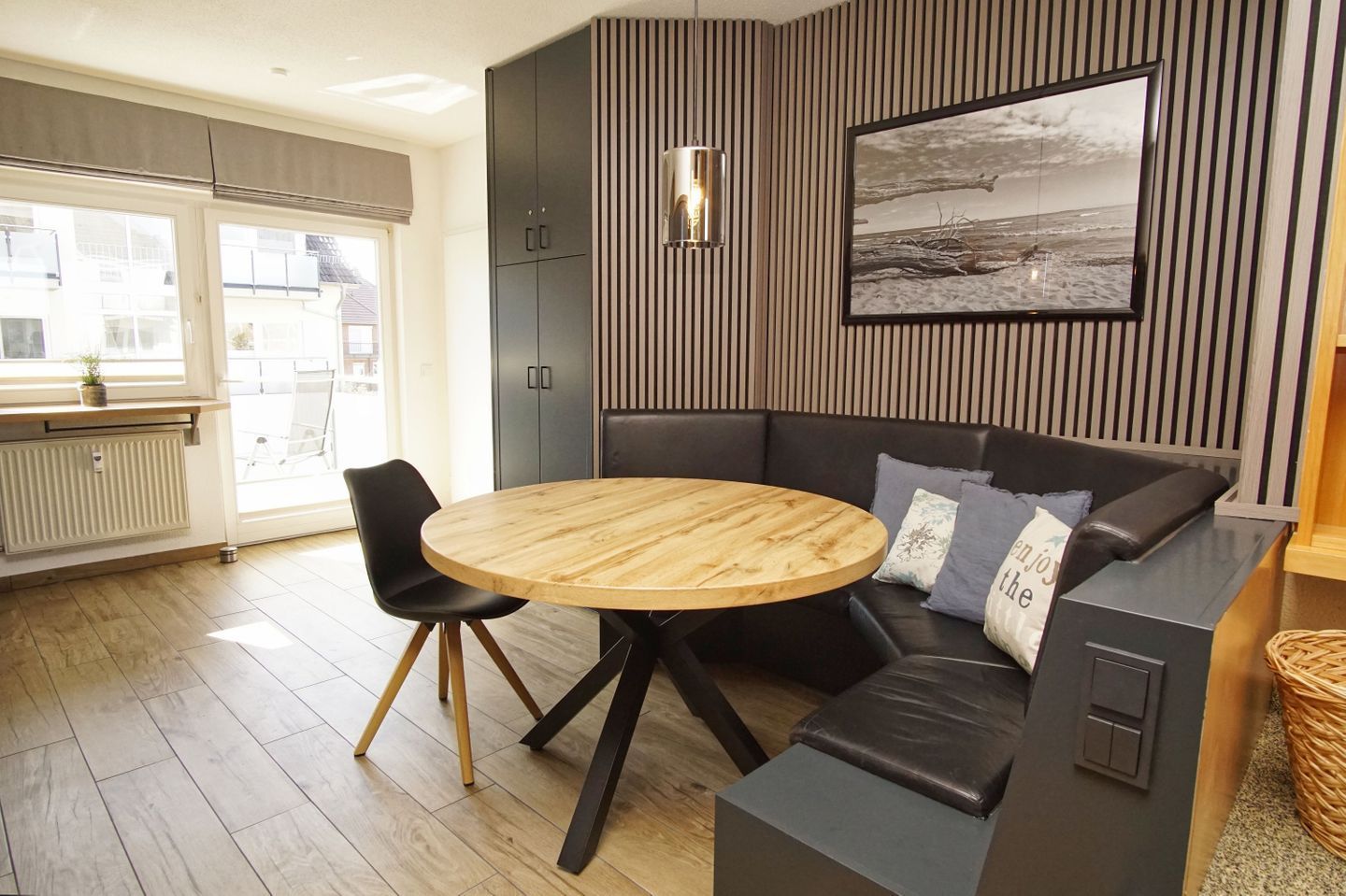 En moderne stue med et rundt træbord, en sort lædersofa og et stort billed i ramme på væggen.