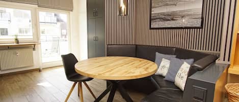 En moderne stue med et rundt træbord, en sort lædersofa og et stort billed i ramme på væggen.