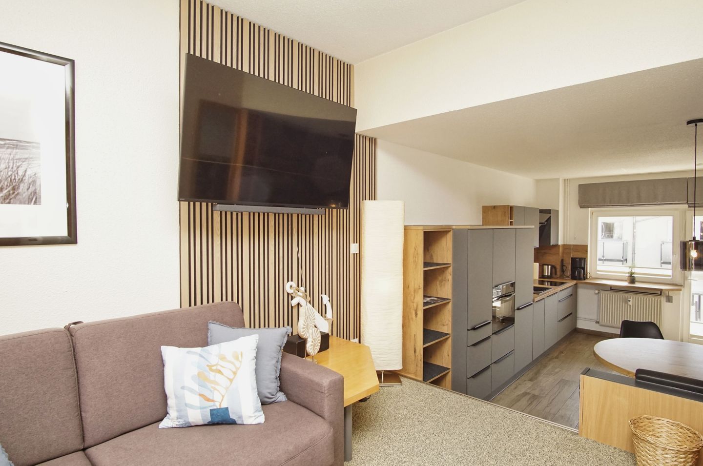 A modern living room with a sofa, a flat-screen TV, and a kitchen with cabinets and a dining area.