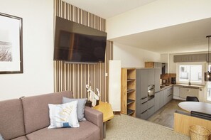 A modern living room with a sofa, a flat-screen TV, and a kitchen with cabinets and a dining area. - Just 100 m from the beach, apartment with a balcony - Apt. Eldena FeWo 15 - Apartments (Middelhagen)