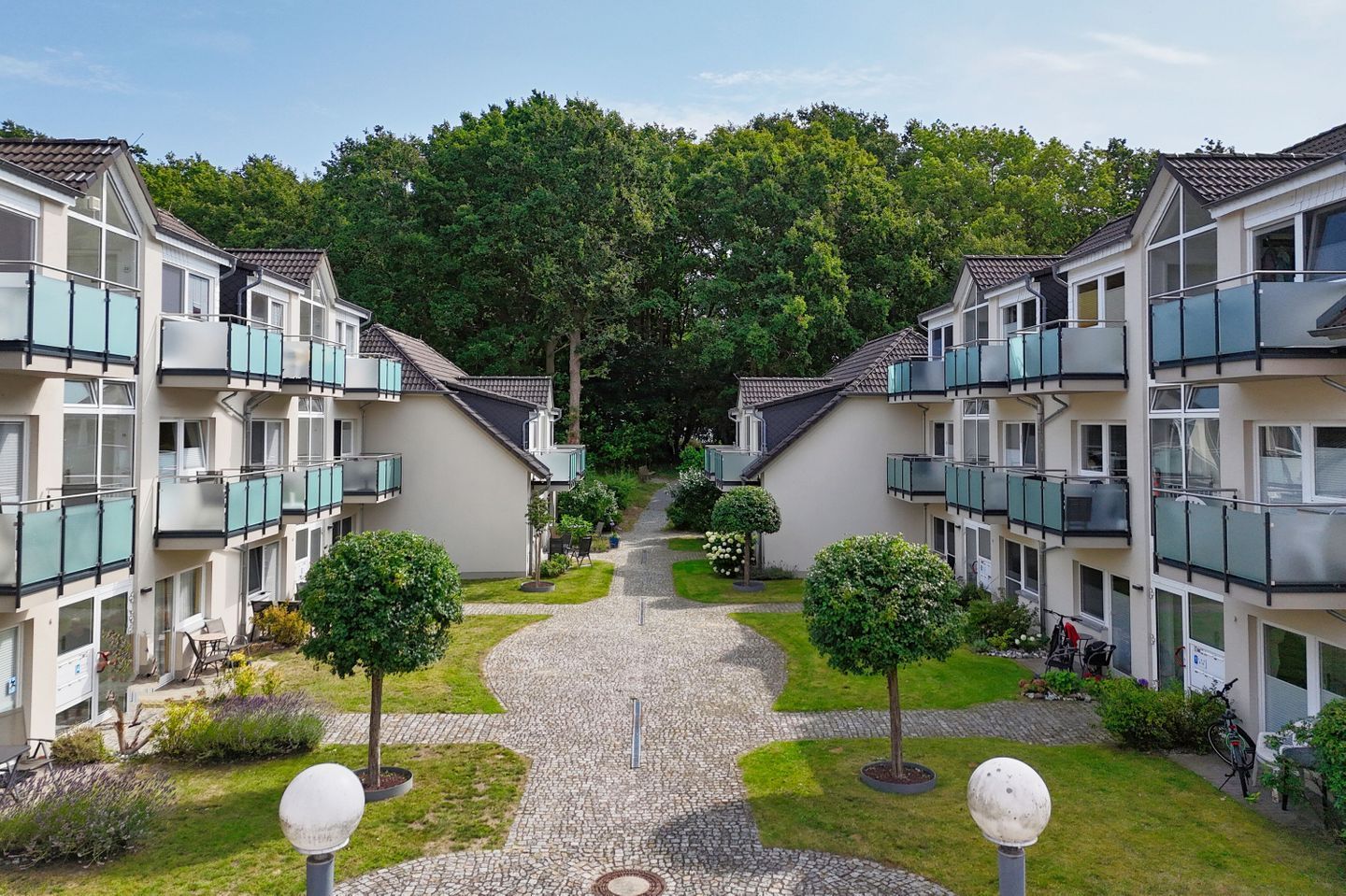 Een rij moderne appartementencomplexen met balkons, een centrale pad en verzorgde groenvoorziening.