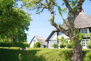 A traditional thatched-roof house with a white exterior and black trim, surrounded by well-maintained hedges and trees. - A Seaside Getaway, Private Swimming Area - Gutshof Ostseeblick FeWo 02 - (Putbus)