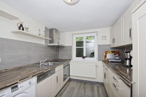A modern kitchen with grey tiles, a built-in oven, a washing machine, and a window with a view of greenery. - Beachfront idyll by the sea, private bathing area - Gutshof Ostseeblick FeWo 02 - (Putbus)