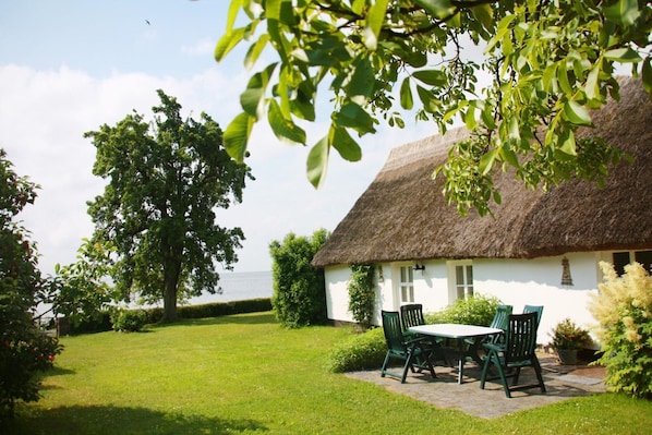 A thatched-roof house with a lawn and a table with chairs. - Beachfront idyll by the sea, private bathing area - Gutshof Ostseeblick FeWo 02 - (Putbus)