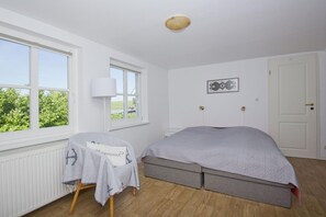 A bedroom with a bed, a chair, a radiator, a window, and a door. - A Seaside Getaway, Private Swimming Area - Gutshof Ostseeblick FeWo 02 - (Putbus)