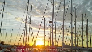 Una marina con diverse barche a vela ormeggiate, un tramonto sullo sfondo e un cielo nuvoloso.