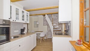 Una cucina compatta con mobili bianchi, un piano di lavoro in legno e un piano cottura integrato. C'è una zona pranzo con tavolo e sedie, e una scala che conduce a un livello superiore.