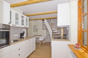 Una cucina compatta con mobili bianchi, un piano di lavoro in legno e un piano cottura integrato. C'è una zona pranzo con tavolo e sedie, e una scala che conduce a un livello superiore.