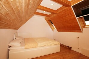 A bedroom with a sloped ceiling, wooden beams, a bed with white bedding, and a window.