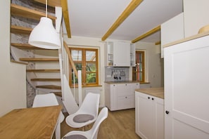 A modern kitchen with white cabinets, a wooden table, and a staircase with wooden beams.