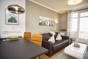A modern living room with a brown leather sofa, wooden chairs, a dining table, and a pendant light.