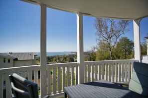 A covered porch with white railings, a table, and a chair, overlooking a residential area with houses and a clear sky. - With sea view and balcony, use of swimming pool and sauna - Sea view apartment 25 - (Göhren)