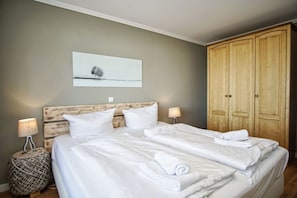 A neatly made bed with white linens and pillows, a wooden headboard, a wall-mounted picture, and a wooden wardrobe.