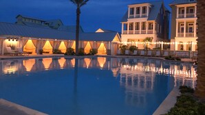 A pool area with a reflection of buildings and lights, surrounded by lounge chairs and a palm tree. - Chic Sunset Views on Palmilla Golf Course, Designer Interior & Chef’s Kitchen (Port Aransas)