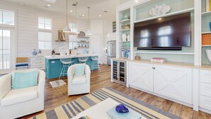 A modern kitchen with a central island, white cabinetry, and a large flat-screen TV above the island. - Chic Sunset Views on Palmilla Golf Course, Designer Interior & Chef’s Kitchen (Port Aransas)