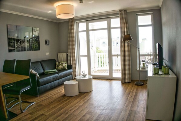 A living room with a green sofa, a wooden dining table, a white coffee table, and a white cabinet.