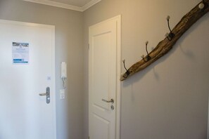 A hallway with two white doors, one with a phone and a sign, and a rustic wooden beam with hooks on the wall.