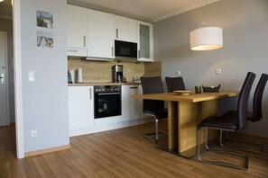 A compact kitchen with white cabinets, a microwave, an oven, and a coffee maker. There is a wooden dining table with four chairs. - With sea view and balcony, use of swimming pool and sauna - Sea view apartment 22 - (Göhren)