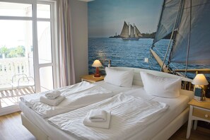 A double bed with white linens, two bedside tables with lamps, a large window with curtains, and a mural of a sailboat on the wall.