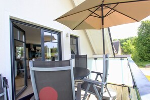 A balcony with a table and chairs, a large umbrella, and a glass door leading to an interior space.