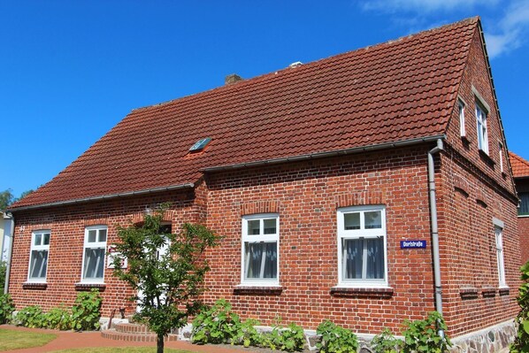 A red-brick building with a tiled roof, a sign reading "Dortstrasse," and a small tree in the foreground.