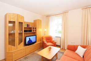 Una sala de estar con televisor, un sofá, una silla y armarios de madera con puertas de vidrio.