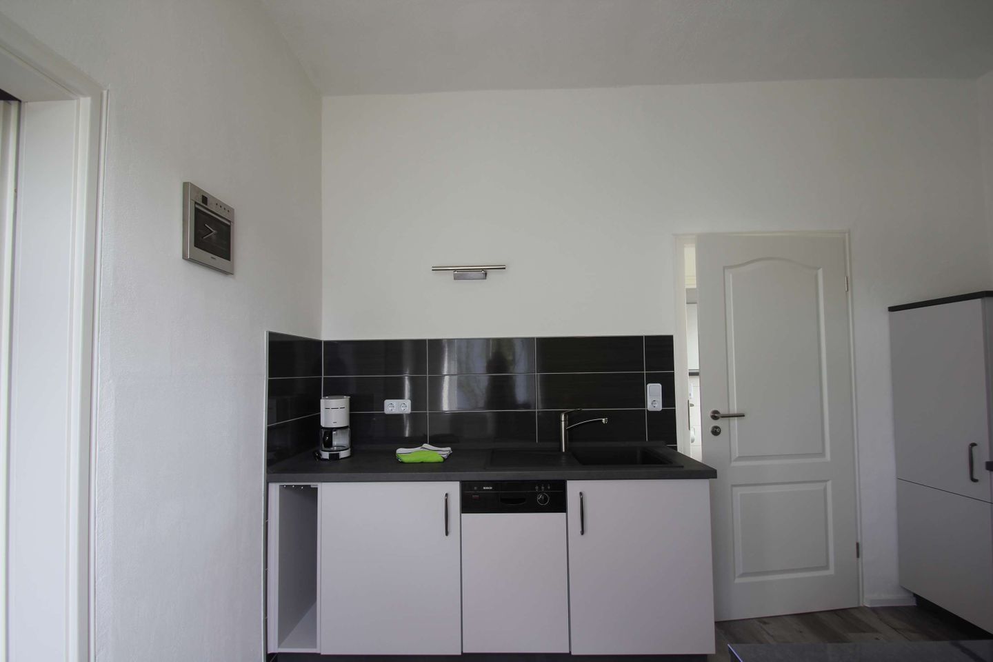 A compact kitchen with a black countertop, white cabinets, and a built-in dishwasher.