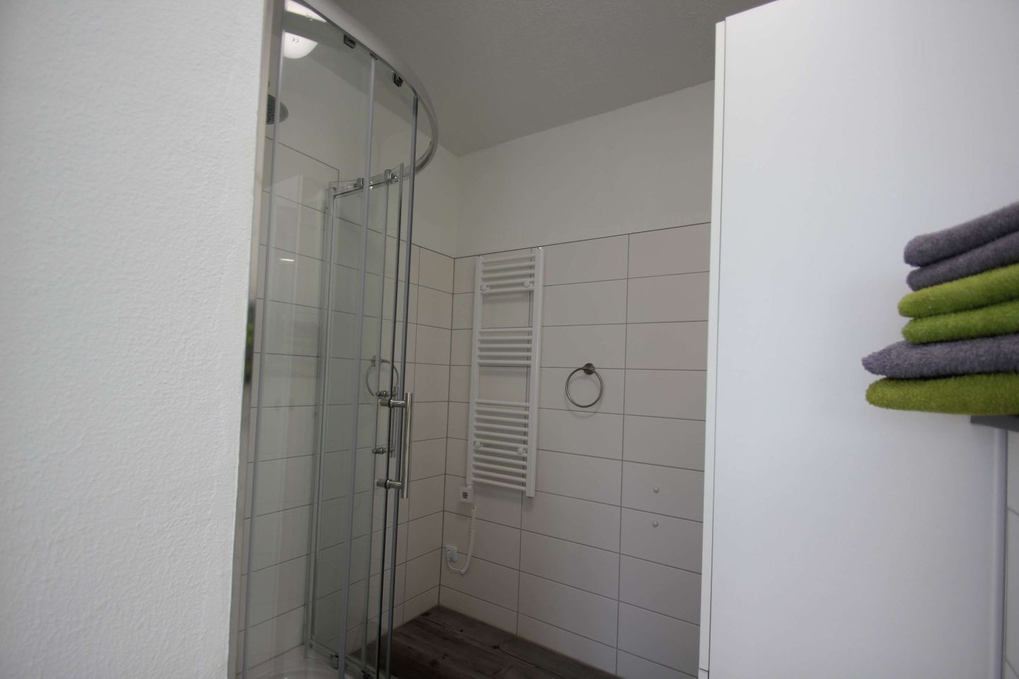 Ein Badezimmer mit Duschkabine aus Glas, weißen Fliesen und einem Handtuchhalter mit mehreren Handtüchern.
