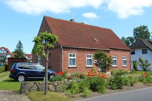 A brick house with a red-tiled roof, a stone wall, and a garden with red flowers. - F-1005 Adonisröschen - Ferienwohnung Adonisröschen F-1005 (Baabe)