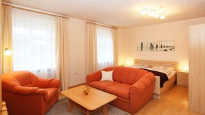 A cozy hotel room with a bed, two orange armchairs, a wooden coffee table, and a nightstand with a lamp. - F-1005 Adonisröschen - Ferienwohnung Adonisröschen F-1005 (Baabe)