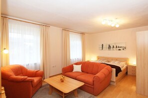 Une chambre d’hôtel confortable, avec un lit, deux fauteuils orange, une table basse en bois et une table de chevet avec une lampe.