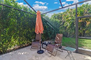 A covered outdoor seating area with two chairs and a table, surrounded by lush greenery. - Pool Home Near Beaches and Downtown 5th Ave. (Naples)