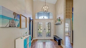 A spacious hallway with wooden flooring, a bench, a chandelier, and a door with glass panels. - Pool Home Near Beaches and Downtown 5th Ave. (Naples)