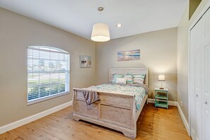 Ein Schlafzimmer mit Bett, Fenster mit Jalousien, Nachttisch und Wandlampe.