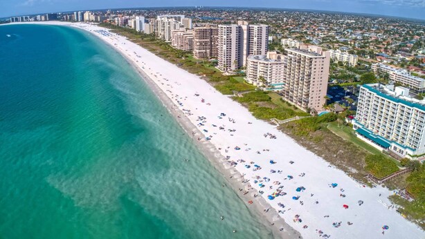 An aerial view of a coastal area with a long sandy beach, high-rise buildings, and a clear blue sea. - Pool Home Near Beaches and Downtown 5th Ave. (Naples)