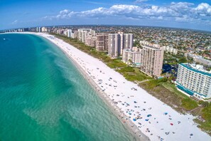 An aerial view of a coastal area with a long sandy beach, high-rise buildings, and a clear blue sea. - Pool Home Near Beaches and Downtown 5th Ave. (Naples)