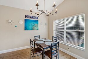 A dining area with a table, chairs, a chandelier, a window with blinds, and wall decorations including a sign and starfish. - Pool Home Near Beaches and Downtown 5th Ave. (Naples)
