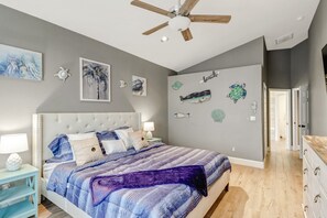 A bedroom with a bed, a ceiling fan, wall art, and a dresser.