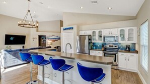 A modern kitchen with a central island, bar stools, and a dining area with a sofa. - Pool Home Near Beaches and Downtown 5th Ave. (Naples)