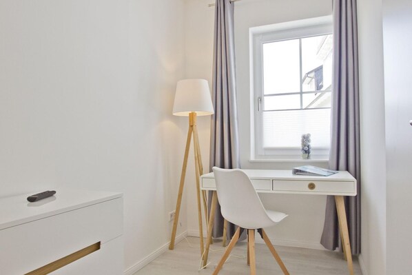 A modern bedroom with a white desk, a white chair, a floor lamp, and a window with curtains.
