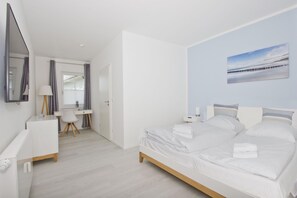 A modern bedroom with a large bed, a desk, and a chair. - Modern vacation apartment with private terrace - Haus Inselwind FeWo MEERsalz - House (Gager)