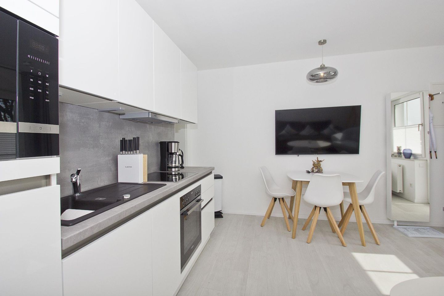 Una cocina moderna con horno integrado, cafetera y comedor con mesa y sillas.