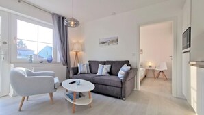 A modern living room with a grey sofa, white armchair, and a round coffee table. A floor lamp and a painting are on the wall. - Modern vacation apartment with private terrace - Haus Inselwind FeWo MEERküste - (Gager)