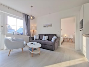 A modern living room with a grey sofa, white armchair, and a round coffee table. A floor lamp and a painting are on the wall. - Modern vacation apartment with private terrace - Haus Inselwind FeWo MEERküste - (Gager)