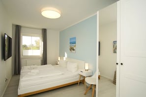 A bedroom with a bed, bedside tables, a ceiling light, a window with curtains, and a painting on the wall. - Modern vacation apartment with a private terrace - Haus Inselwind FeWo MEERstille - (Gager)