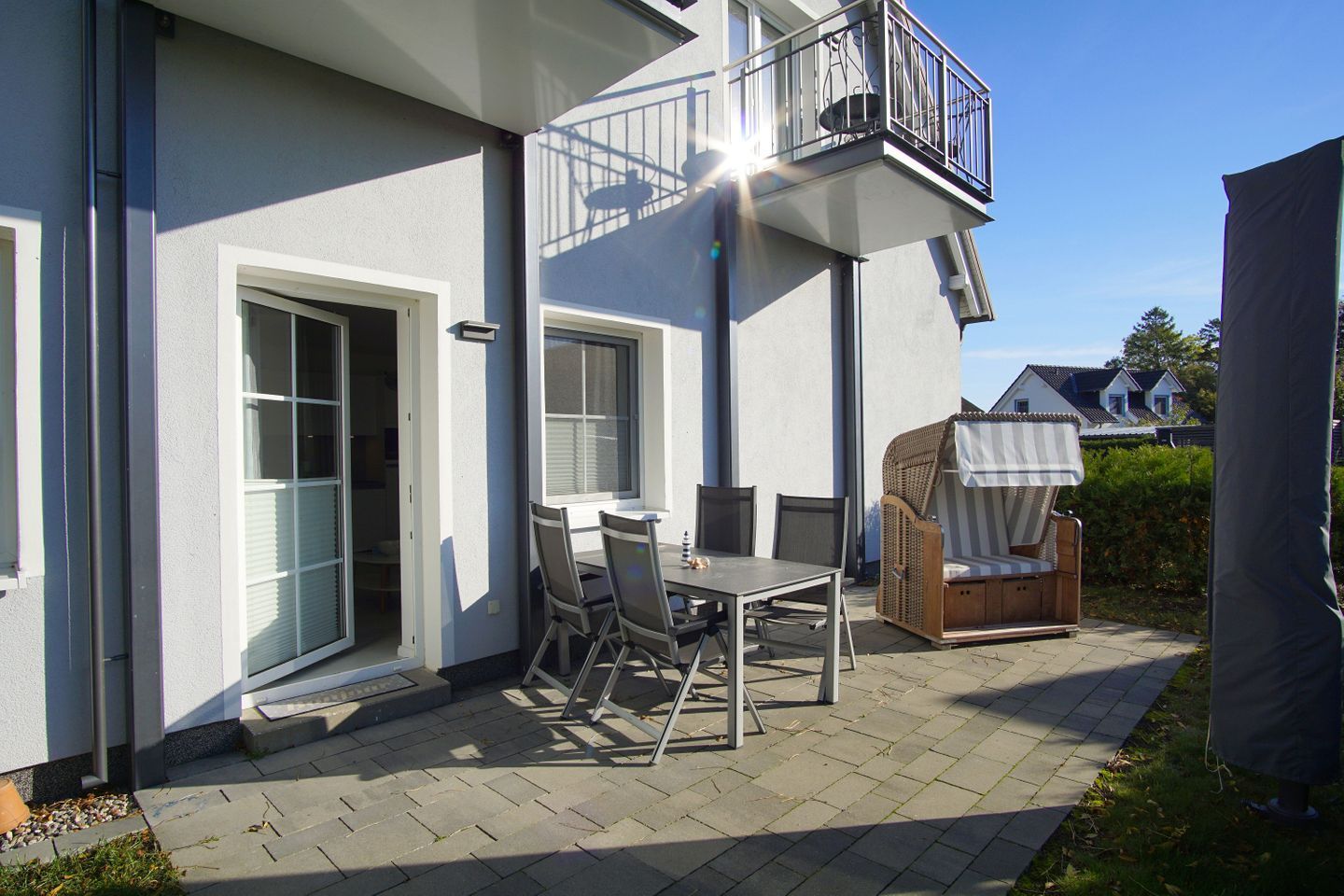 A house with a patio area featuring a table and chairs, a wicker sofa, and a balcony with a railing.