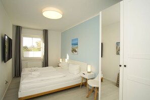 A bedroom with a bed, bedside tables, a ceiling light, a window with curtains, and a painting on the wall. - Modern vacation apartment with private terrace - Haus Inselwind FeWo MEERstille - (Gager)