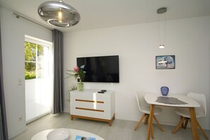 Un salon moderne doté d’un téléviseur à écran plat, d’un canapé blanc, d’une table à manger avec des chaises et d’un vase décoratif.