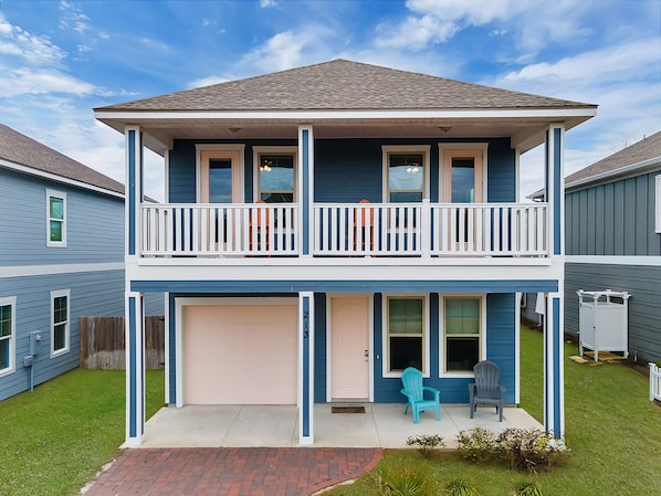 Un immeuble résidentiel de deux étages, doté d’un garage à l’avant, d’un balcon avec des balustrades et d’une petite pelouse avec deux chaises.