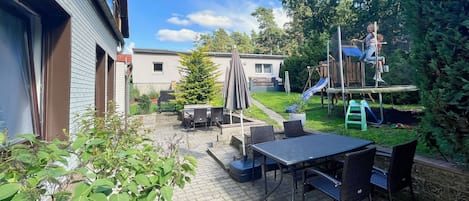 En patio med bord og stole, en lille legeplads og en rutchebane.